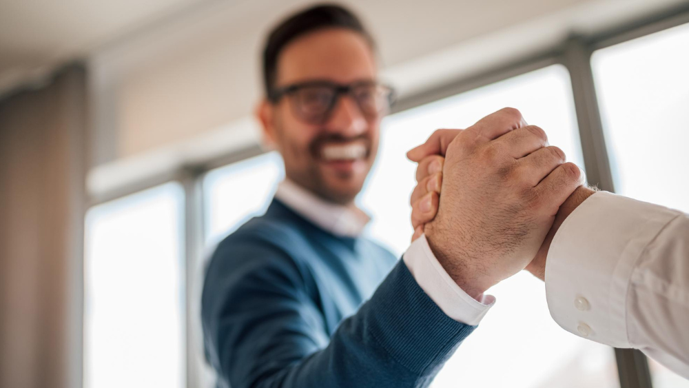 Agente de seguros estrechando la mano de un cliente con confianza al presentar su producto